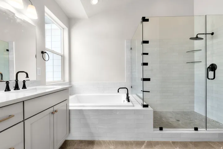 Modern bathroom featuring a dual vanity with white cabinetry and light-toned countertops, a built-in soaking tub with subway tile surround, and a glass-enclosed shower with black hardware and an integrated rain shower head
