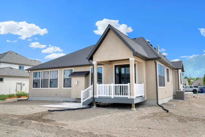 Stucco exterior featuring a covered deck with white railings, a concrete patio, and a dark shingled roof