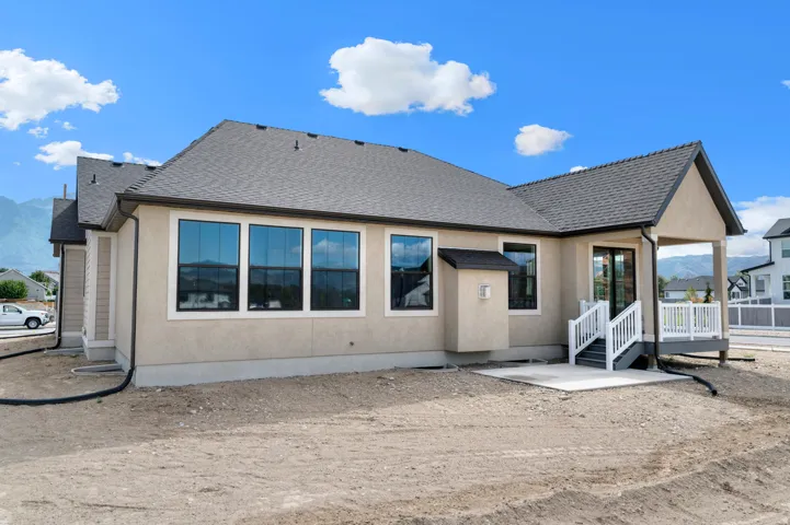 Rear exterior featuring a covered patio with white railing and stairs, a concrete patio area, multiple large windows, and a neutral stucco facade