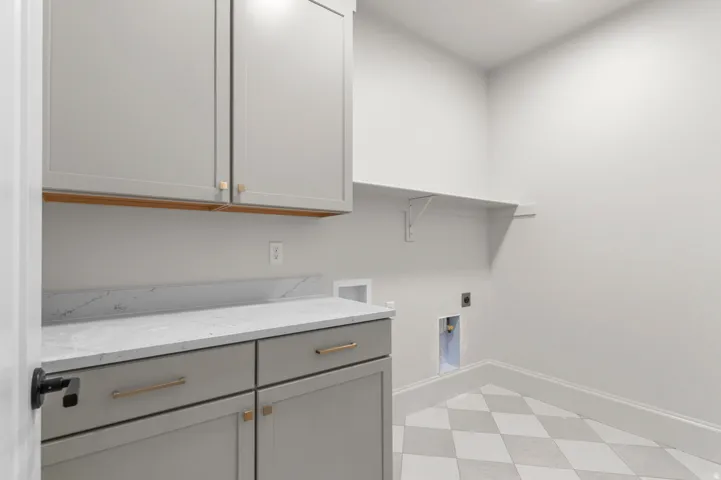 Laundry room featuring light gray cabinetry with gold-toned hardware, a white countertop with subtle veining, and a complementary white backsplash