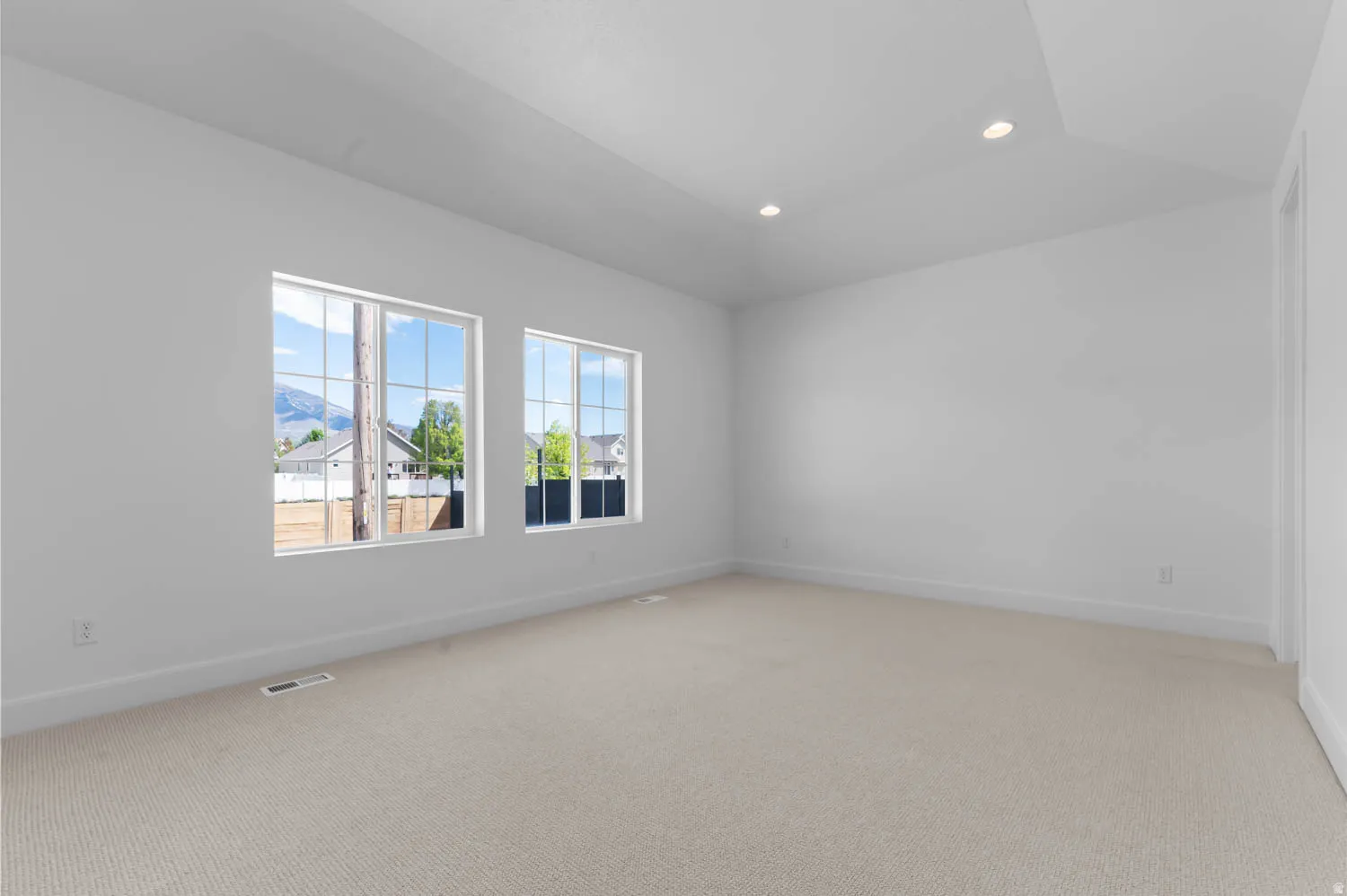 Spacious interior room featuring two large grid windows, recessed ceiling lighting, light-toned carpeting, white walls, and white baseboards