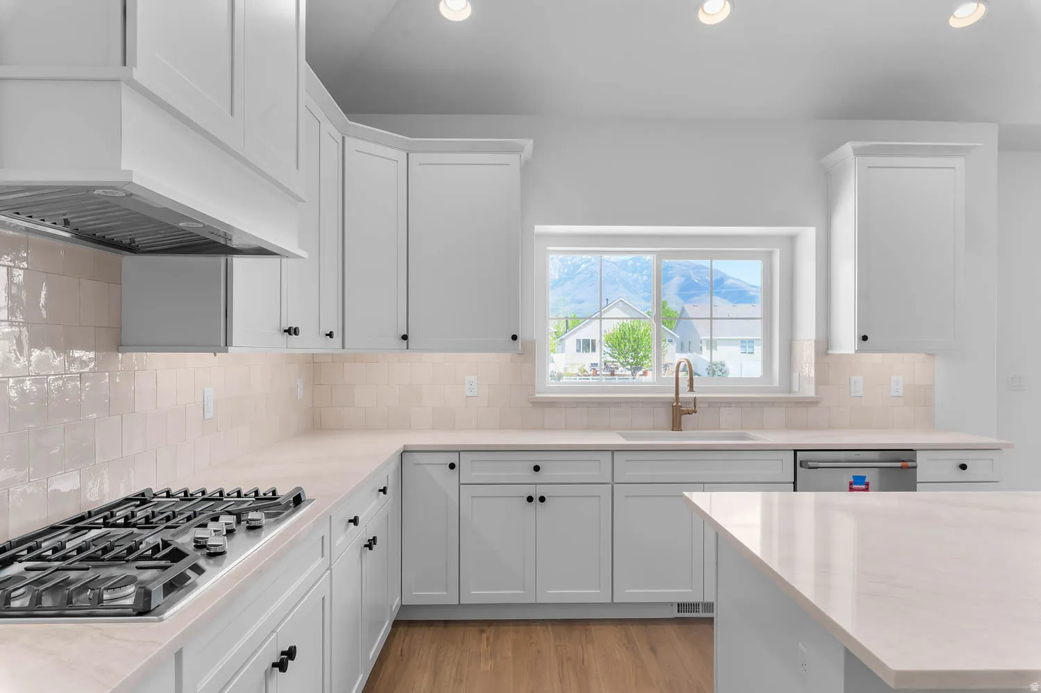 Bright kitchen featuring abundant white cabinetry, light countertops, a gas cooktop, a stainless steel range hood, and a window above the sink