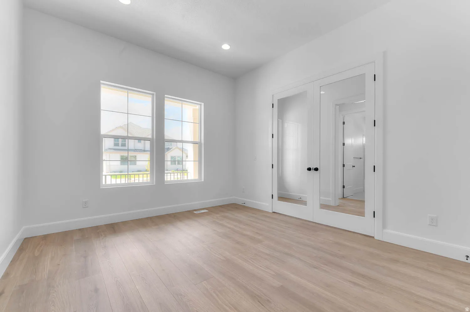 Light-filled room featuring dual windows, recessed lighting, wood-finish flooring, white baseboards, and double French doors