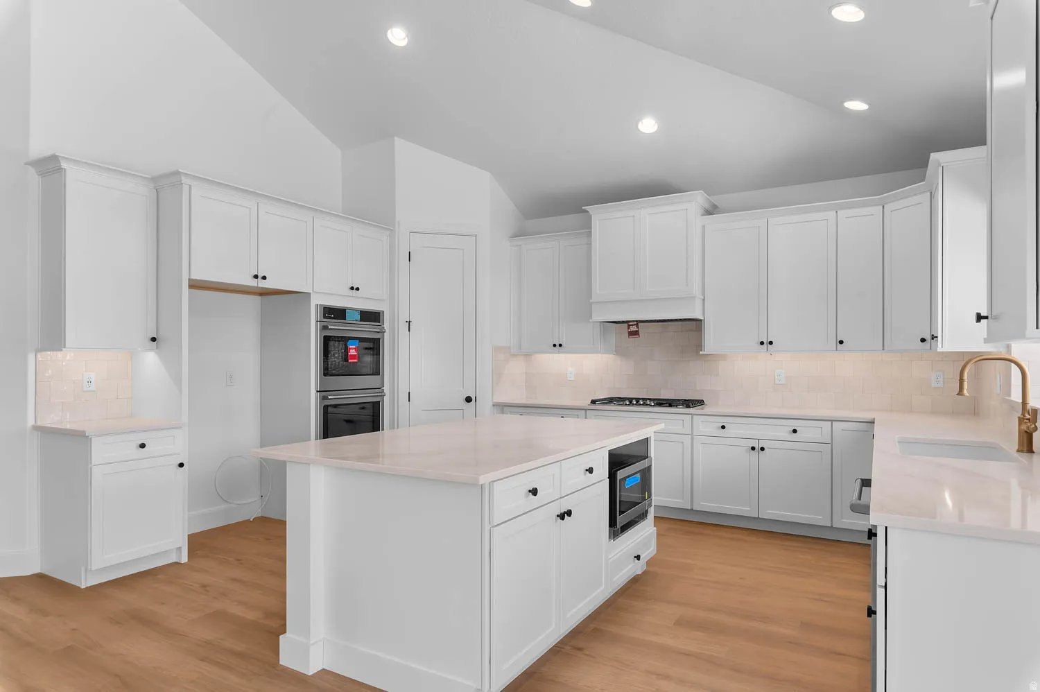 Spacious kitchen featuring white cabinetry, light-toned countertops, and wood-finish flooring