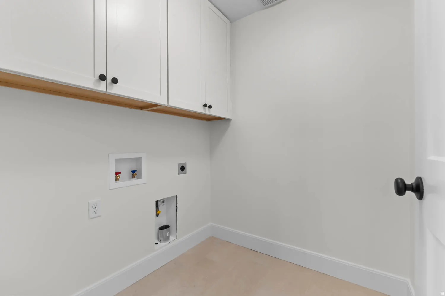 Laundry area featuring white cabinetry with black hardware, a wood-finish shelf, and connections for appliances