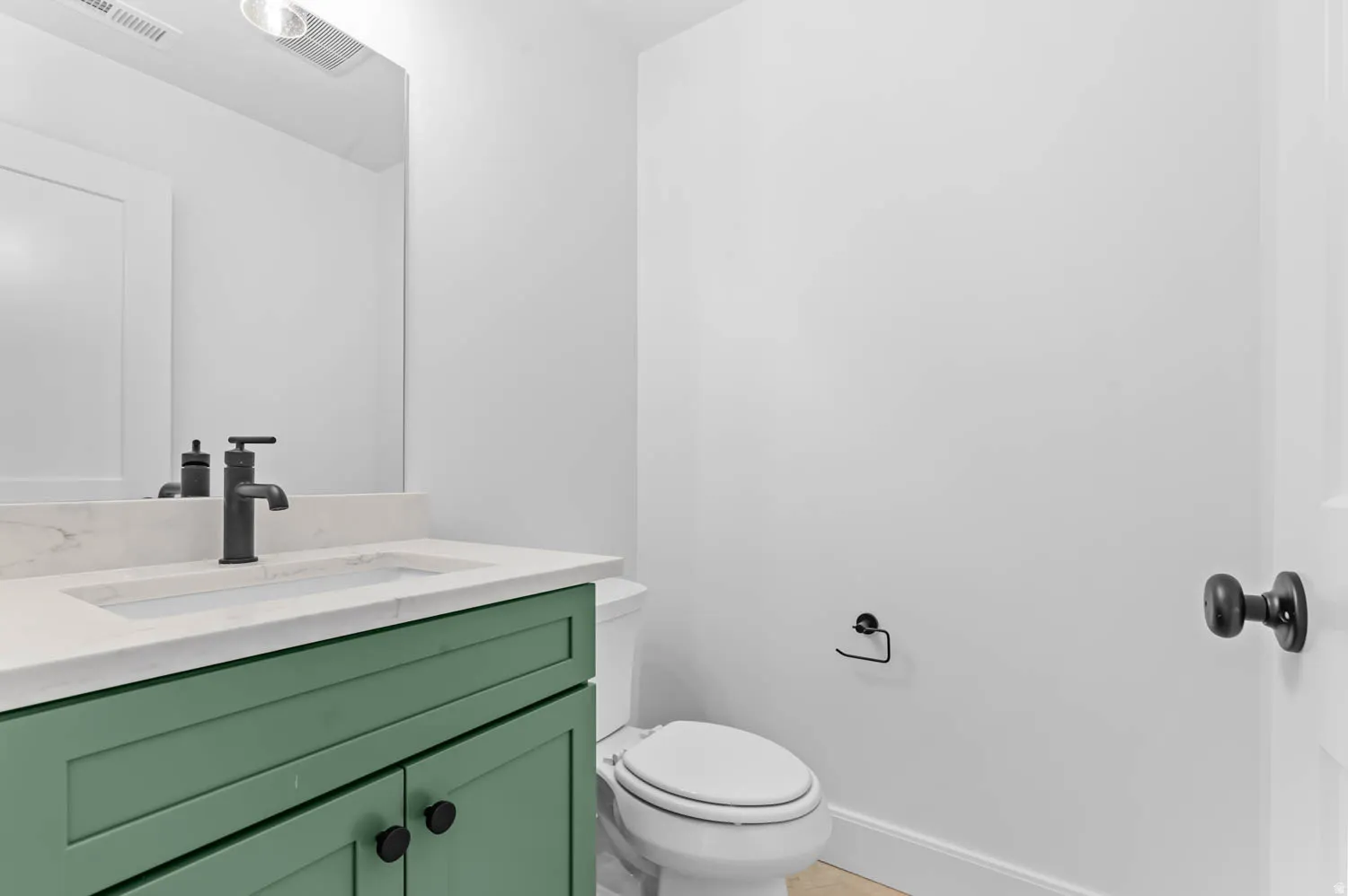 Powder room featuring a green vanity with a light-colored countertop, an undermount sink, and a matte black faucet