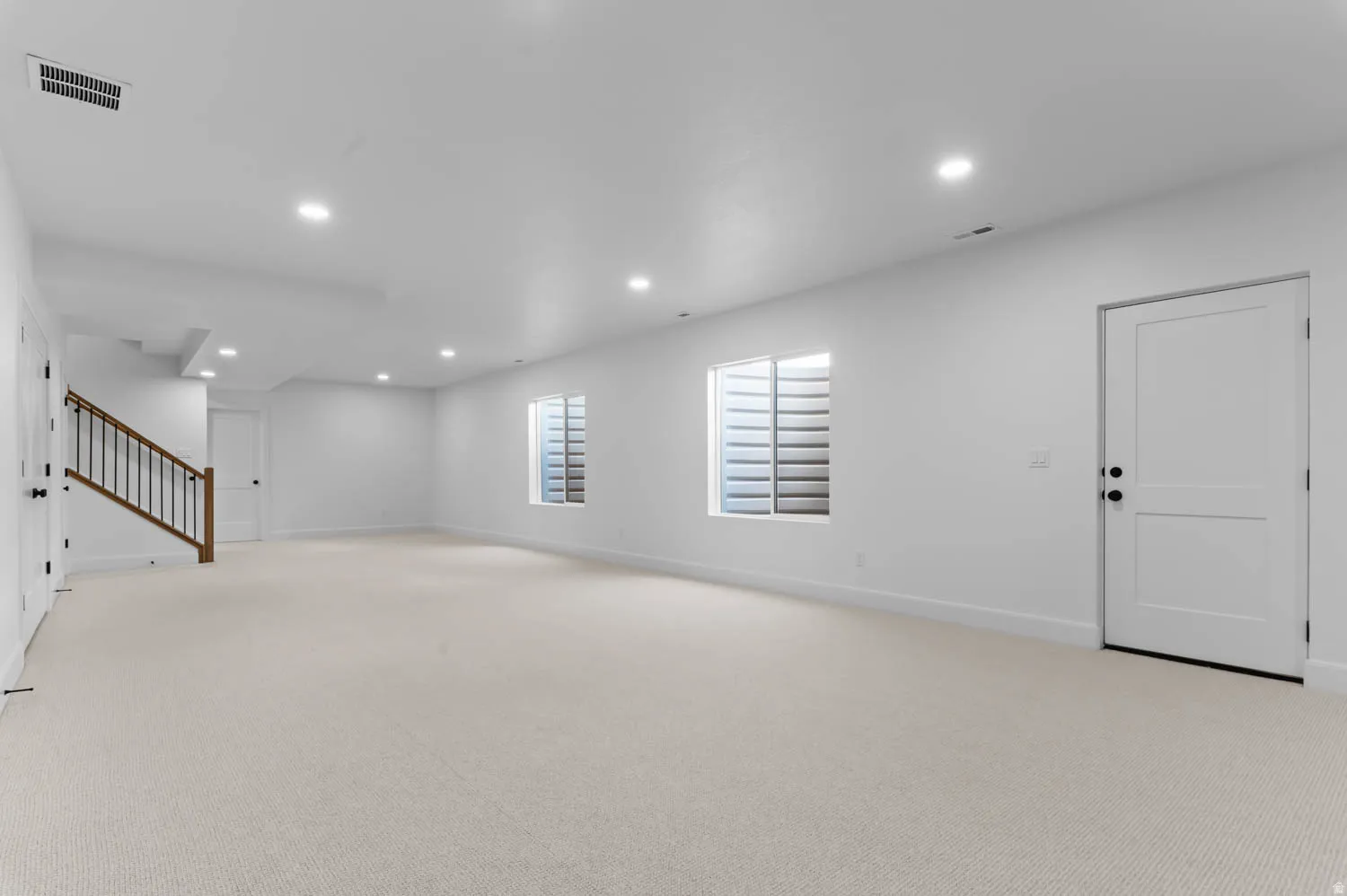 Spacious interior room featuring light-toned carpeting, recessed lighting, and white walls