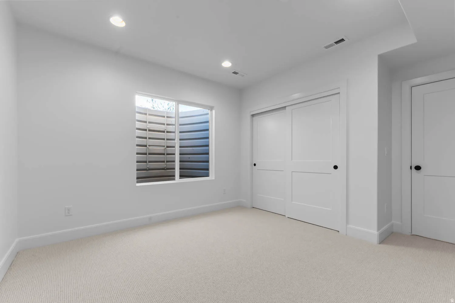 Carpeted room featuring a white window with a window well, recessed lighting, white trim, and a white sliding closet door with black hardware
