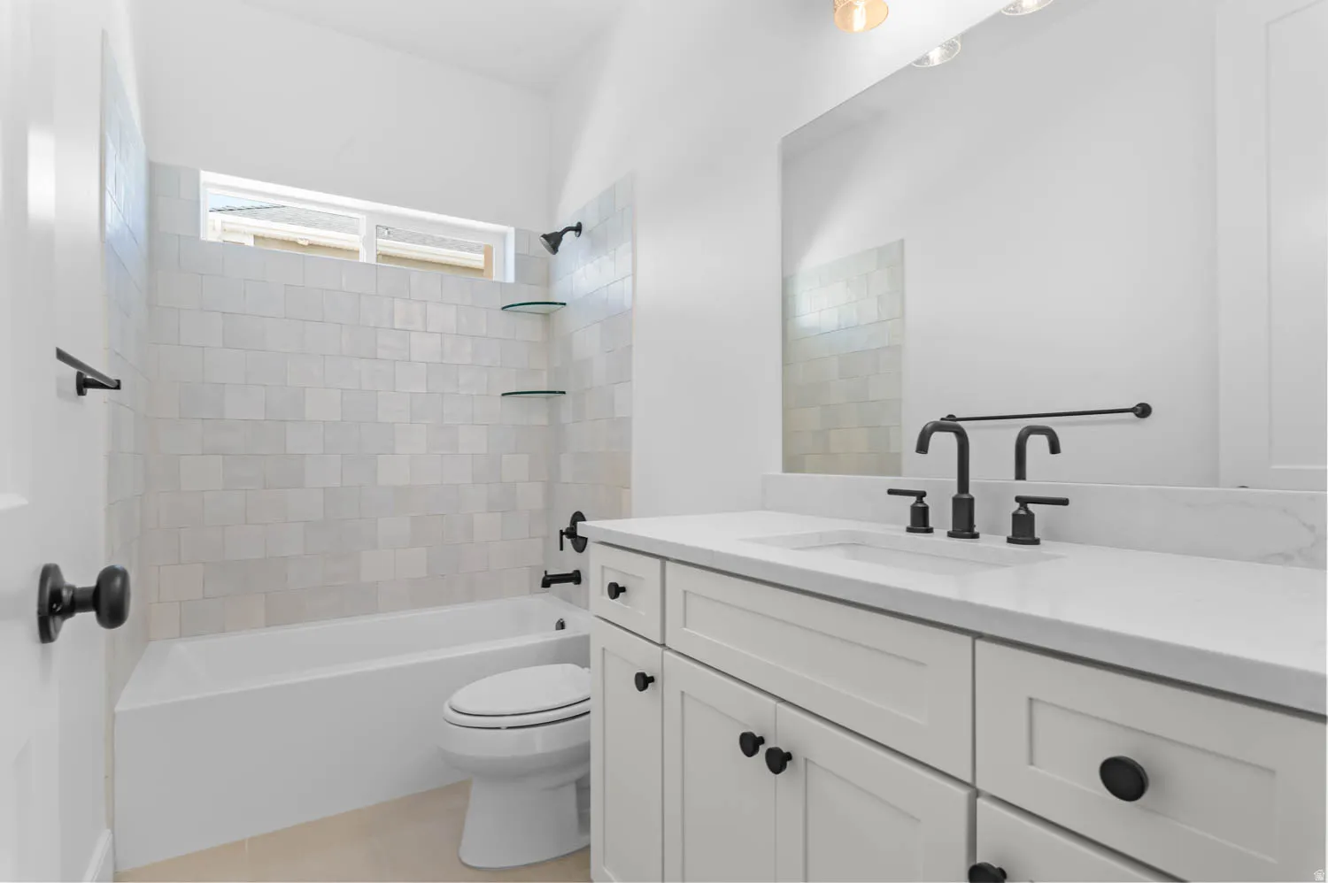 Bathroom featuring a white vanity with a light-colored countertop, matte black fixtures, an integrated tub and shower with light-toned tile surround, and a clerestory window