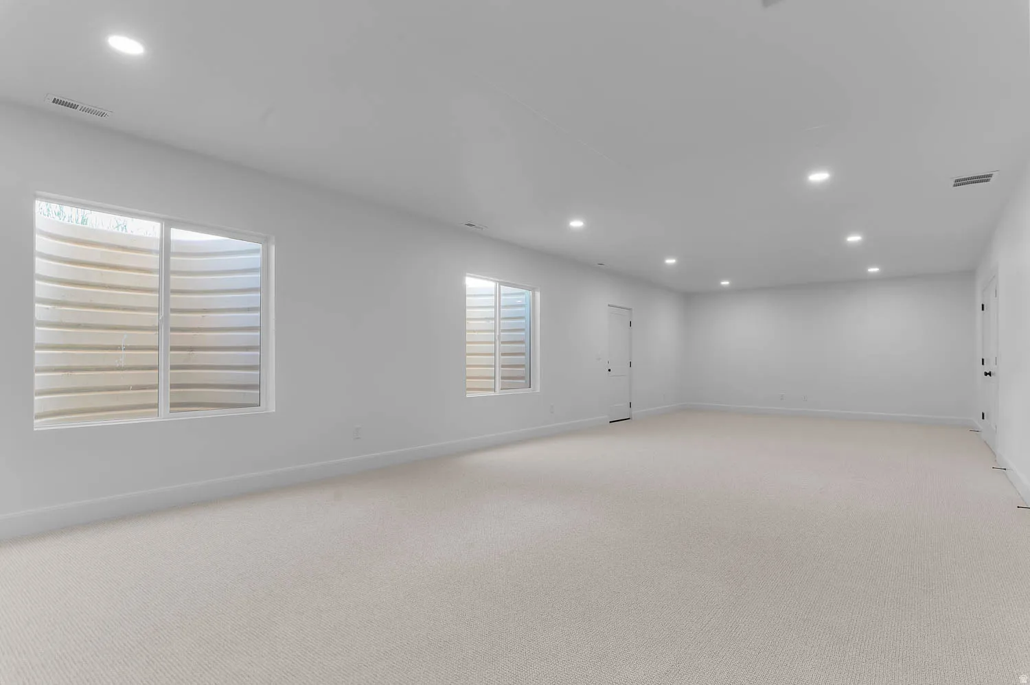Spacious room featuring light-toned carpeting, white walls, and recessed ceiling lighting