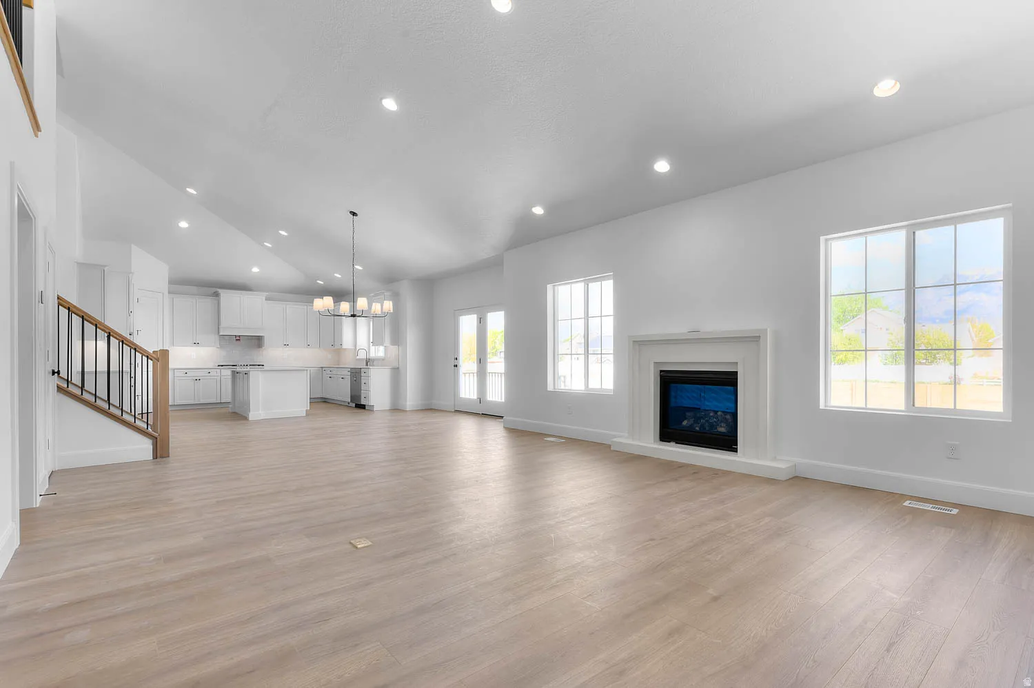 Spacious open-concept living area featuring light wood-finish flooring, a white mantel fireplace, and large windows