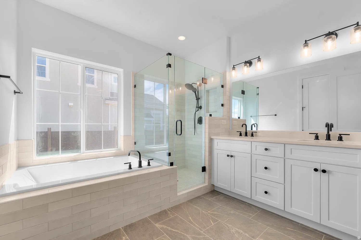 Spacious bathroom featuring a built-in soaking tub, an enclosed glass shower, a dual vanity with undermount sinks, and contemporary light fixtures