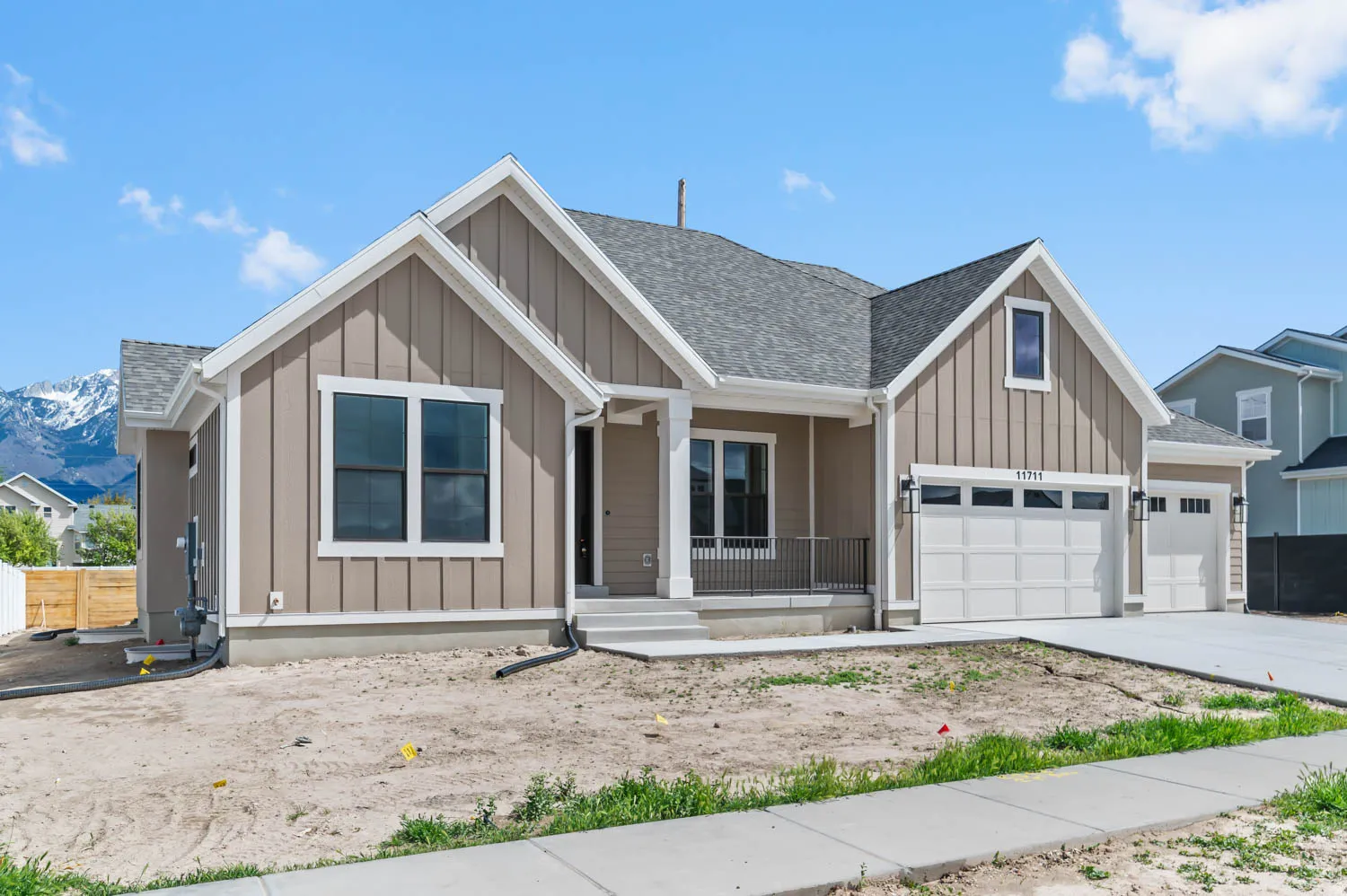 Contemporary ranch-style exterior featuring board and batten siding, a covered porch with a metal railing, and an attached two-car garage with an additional single-car garage
