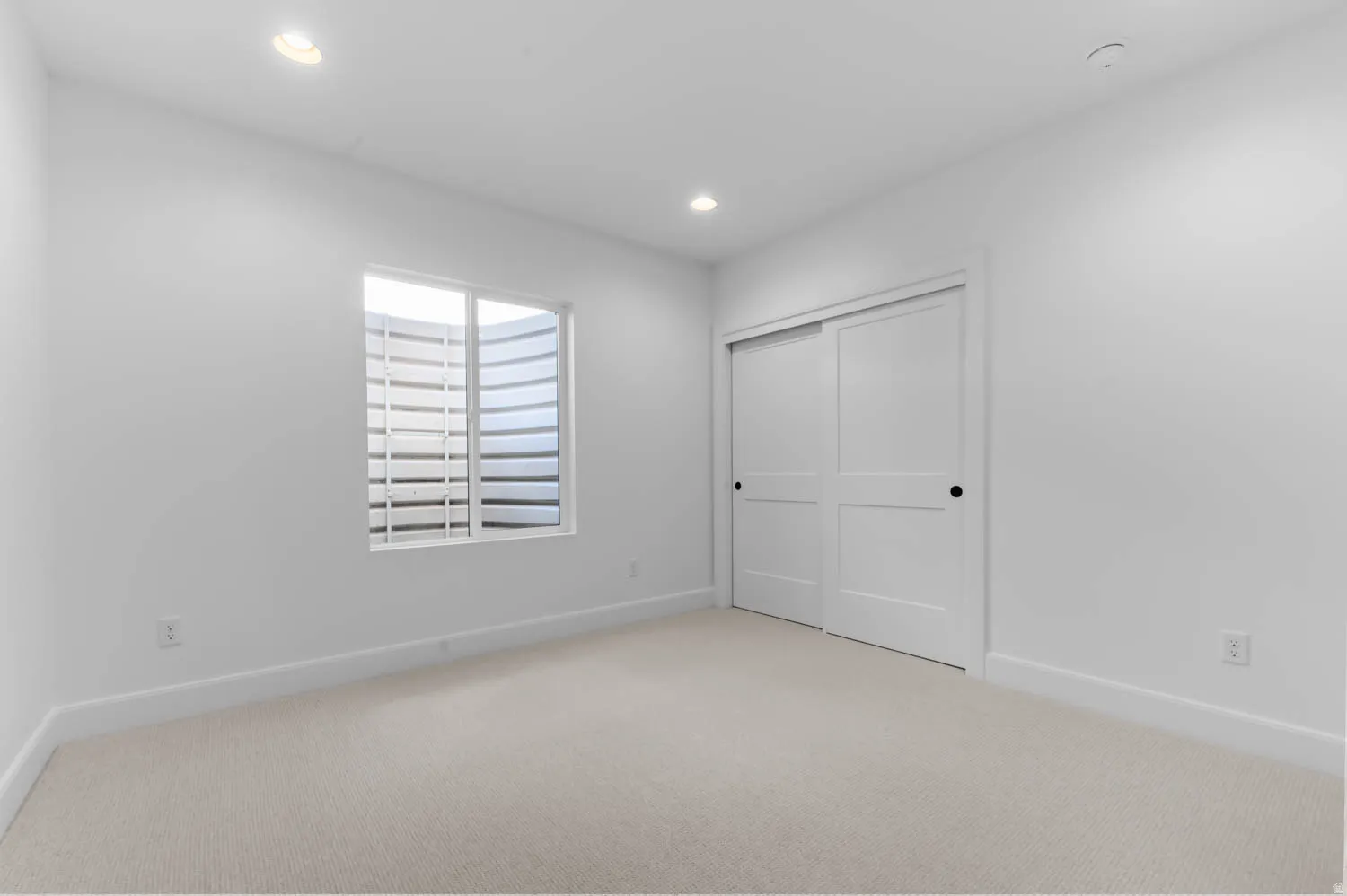 Bright secondary bedroom offering generous square footage with neutral carpet flooring, recessed ceiling lighting, and abundant natural light from a shuttered window
