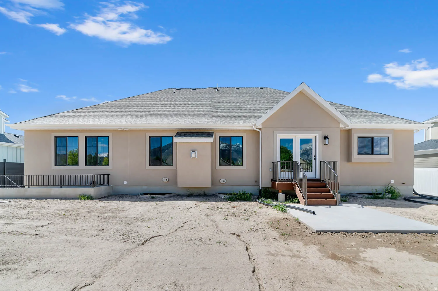 Rear exterior featuring stucco siding, multiple windows with black frames, and a gable accent over double glass doors