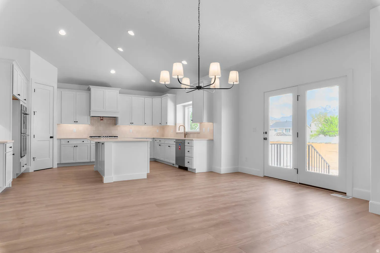 Spacious kitchen and living area featuring wood-finish flooring, white cabinetry, a center island, and double French doors leading to an outdoor deck