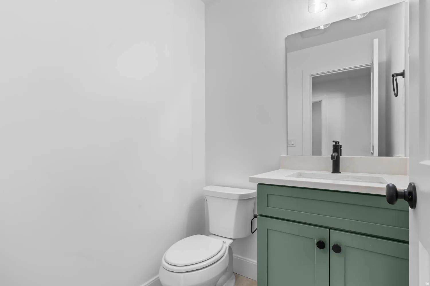 Bathroom vanity featuring a green cabinet, white countertop, and matte black faucet