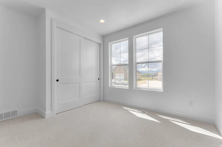 Recessed lighting illuminates a space featuring two large windows, a sliding two-panel closet door, and light-toned carpeting