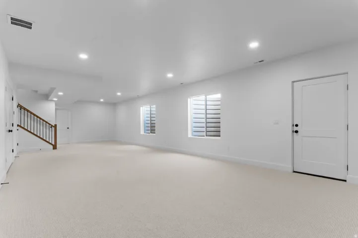 Spacious interior room featuring light-toned carpeting, recessed lighting, and white walls