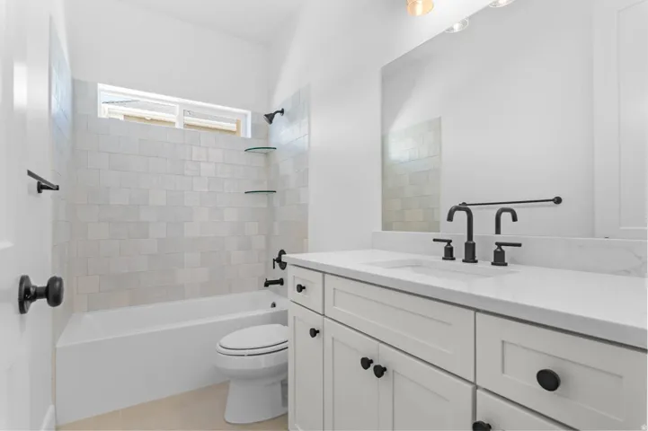 Bathroom featuring a white vanity with a light-colored countertop, matte black fixtures, an integrated tub and shower with light-toned tile surround, and a clerestory window