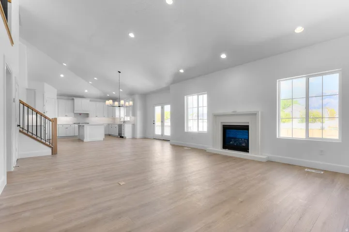 Spacious open-concept living area featuring light wood-finish flooring, a white mantel fireplace, and large windows