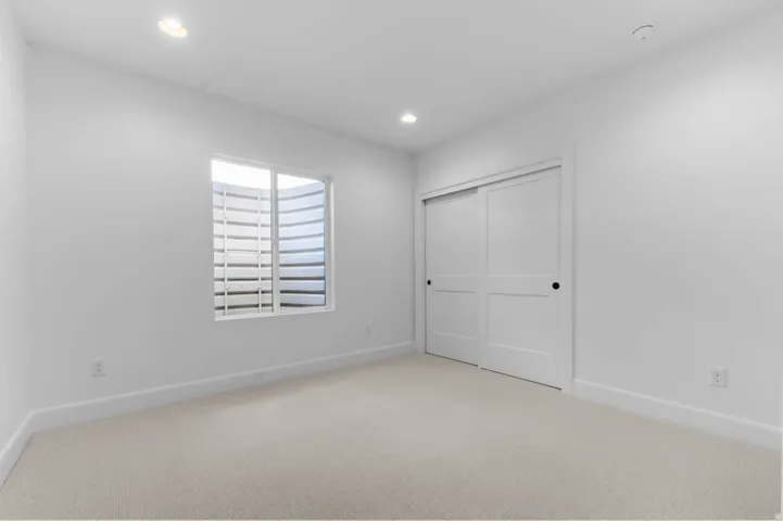Bright secondary bedroom offering generous square footage with neutral carpet flooring, recessed ceiling lighting, and abundant natural light from a shuttered window