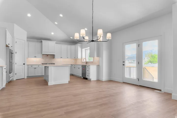 Spacious kitchen and living area featuring wood-finish flooring, white cabinetry, a center island, and double French doors leading to an outdoor deck