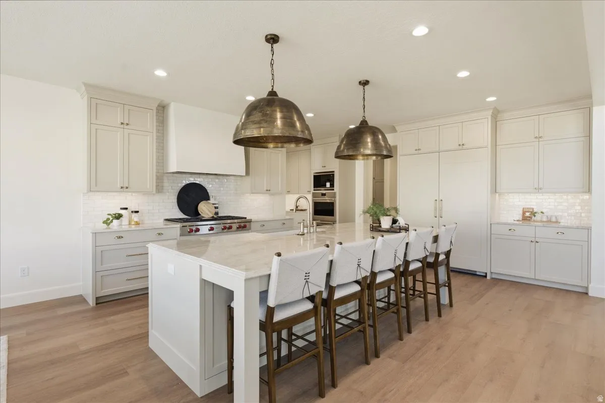 Spacious kitchen featuring a large central island with seating, extensive light-toned cabinetry, integrated paneled refrigerator, a professional-grade range with a custom hood, and wood-finish flooring