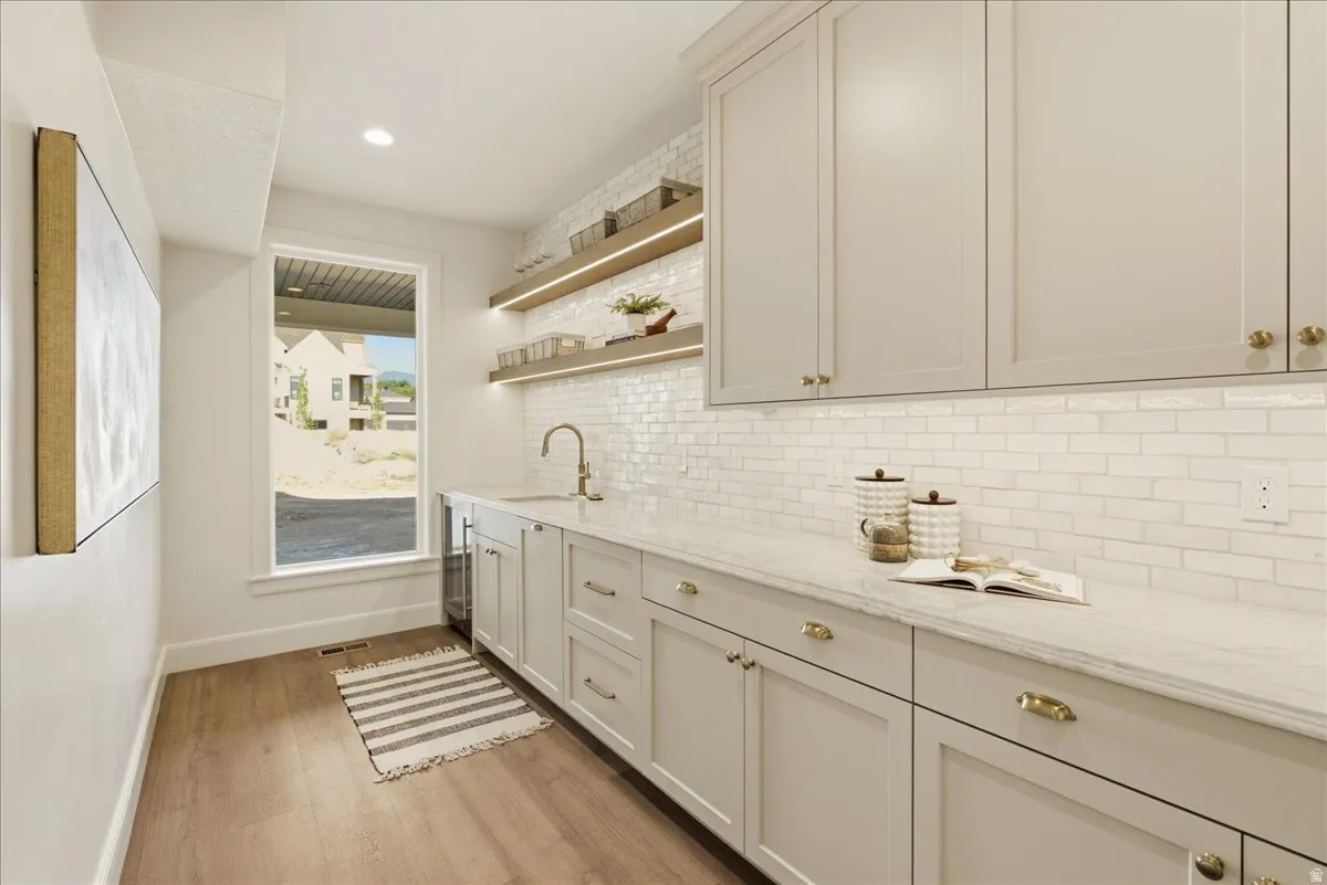 Bright utility space featuring extensive cabinetry, undermount sink with gooseneck faucet, light wood-finish flooring, white subway tile backsplash, and recessed lighting