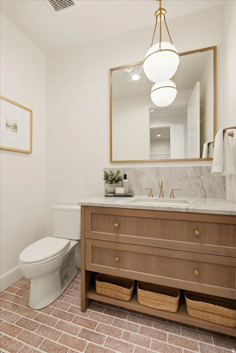 Bathroom featuring a wood-finish vanity with drawer storage, a recessed sink, and a stone-finish countertop