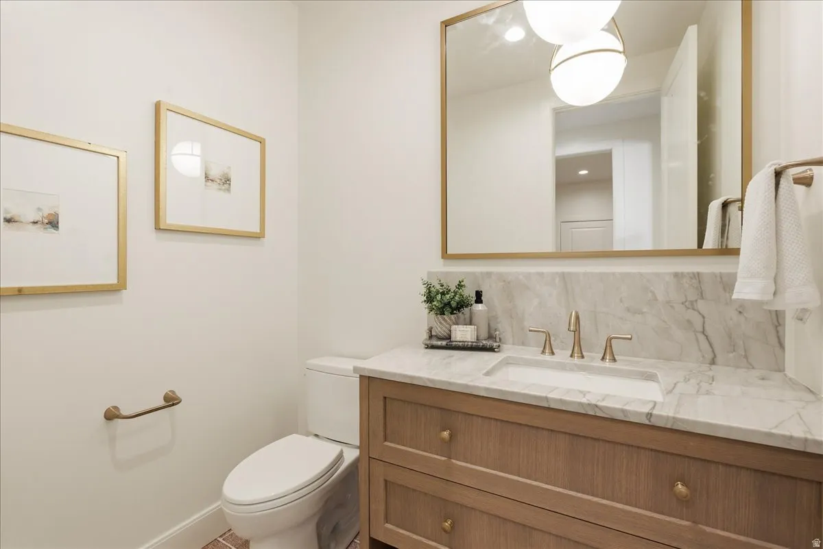 Bathroom featuring a vanity with a stone countertop and integrated sink, a large gold-framed mirror, and a contemporary light fixture