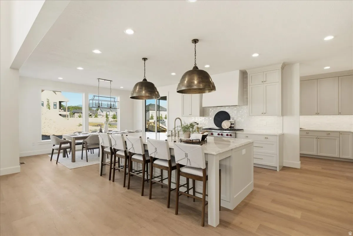 Spacious kitchen featuring a large central island with seating, pendant lighting, professional-grade range, and light wood-finish flooring