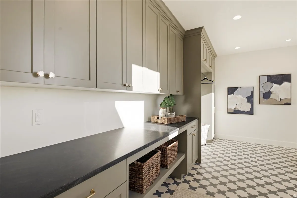 Laundry room featuring extensive built-in cabinetry, dark countertops, recessed lighting, and patterned floor tiles