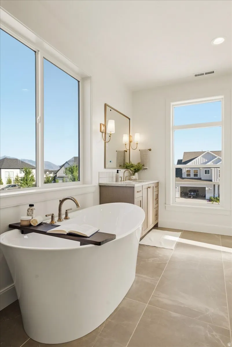 Freestanding soaking tub with a floor-mounted faucet, complemented by a dual-sink vanity with wood-finish cabinetry, a stone countertop, and an integrated backsplash