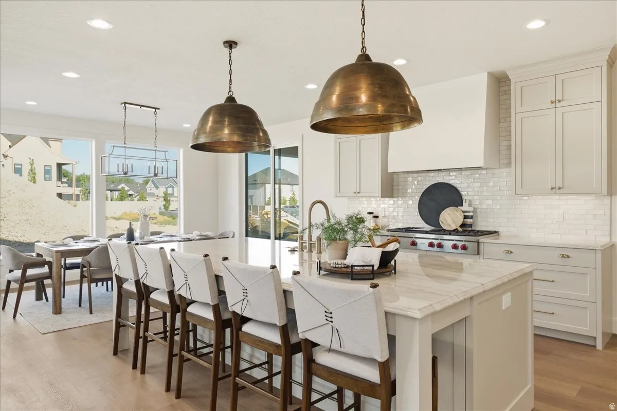 Gourmet kitchen featuring a large central island with seating, a professional-grade range, a white subway tile backsplash, and light wood-finish flooring