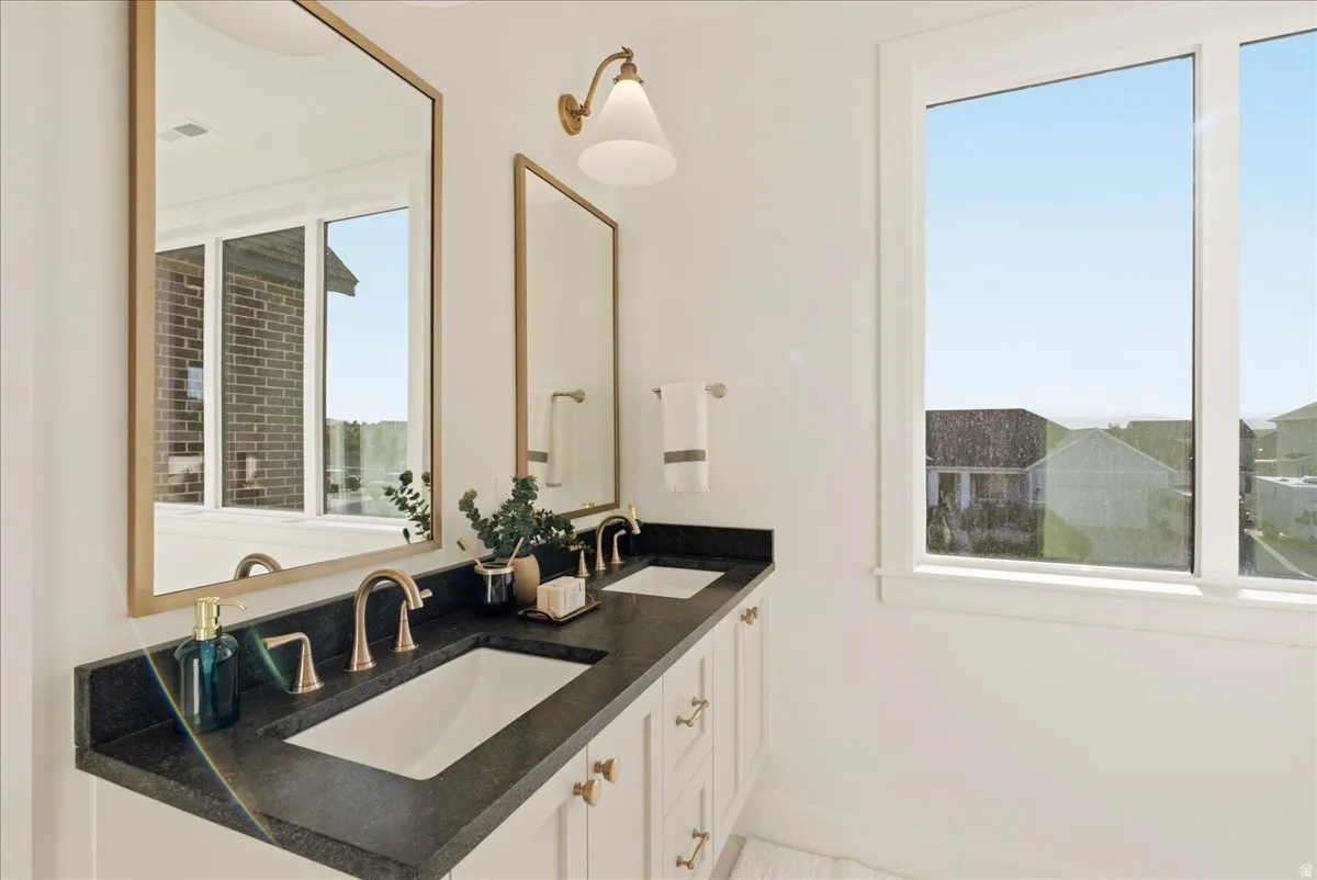 Double vanity featuring a dark countertop, undermount sinks, and brass-finish fixtures