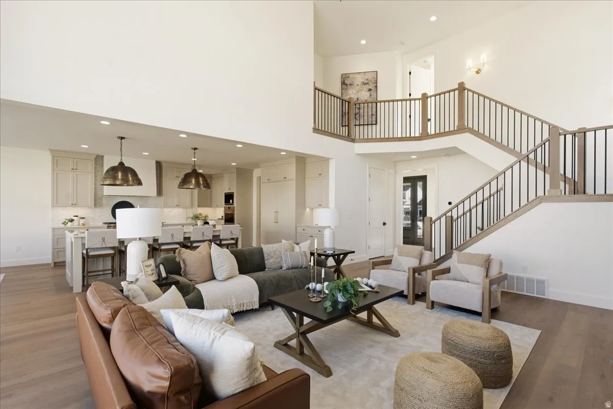 Two-story living area featuring wood-finish flooring, a grand staircase with wood and metal railings, and a soaring ceiling