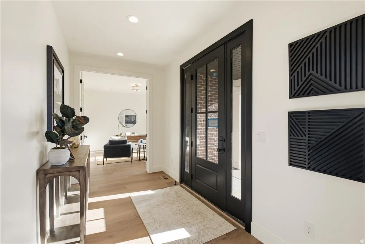 Entryway featuring a dark-framed double door with glass panels, light wood-finish flooring, recessed lighting, and white walls