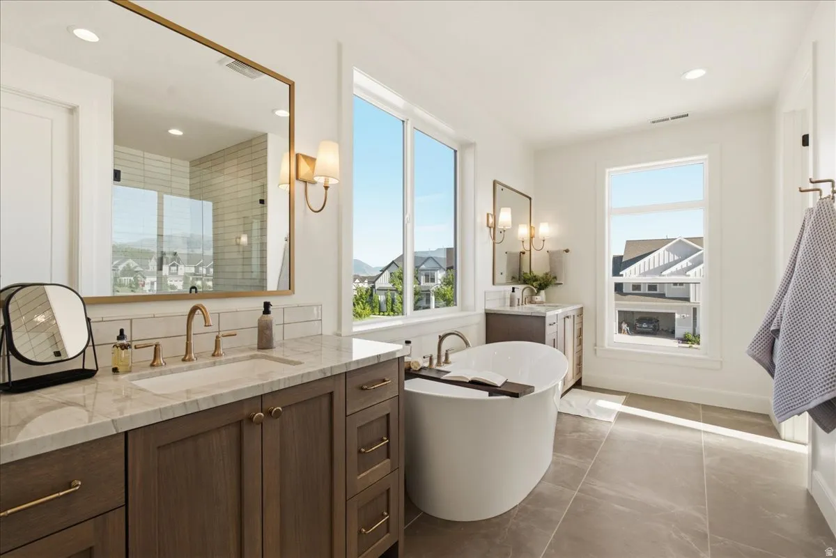 Bright bathroom featuring a freestanding soaking tub, a dual vanity with a stone countertop, a glass-enclosed shower, and large windows