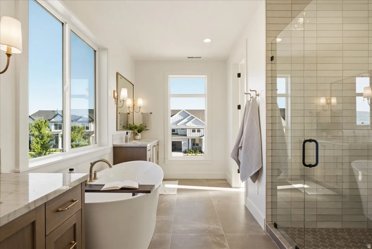 Spacious bathroom featuring a freestanding soaking tub, dual vanities with stone countertops, a large glass-enclosed shower with subway tile, and abundant natural light from multiple windows