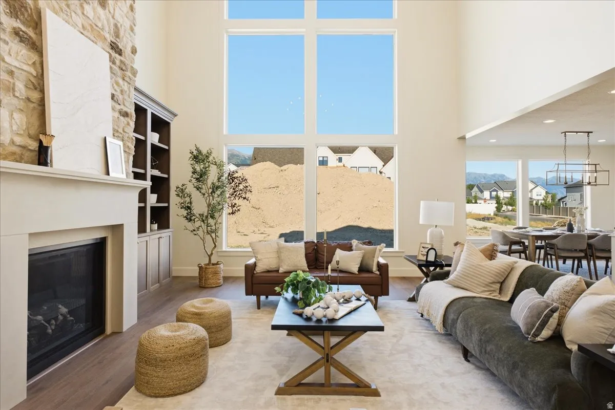 Great room featuring a two-story ceiling, stone-clad fireplace, built-in shelving, wood-finish flooring, and expansive windows