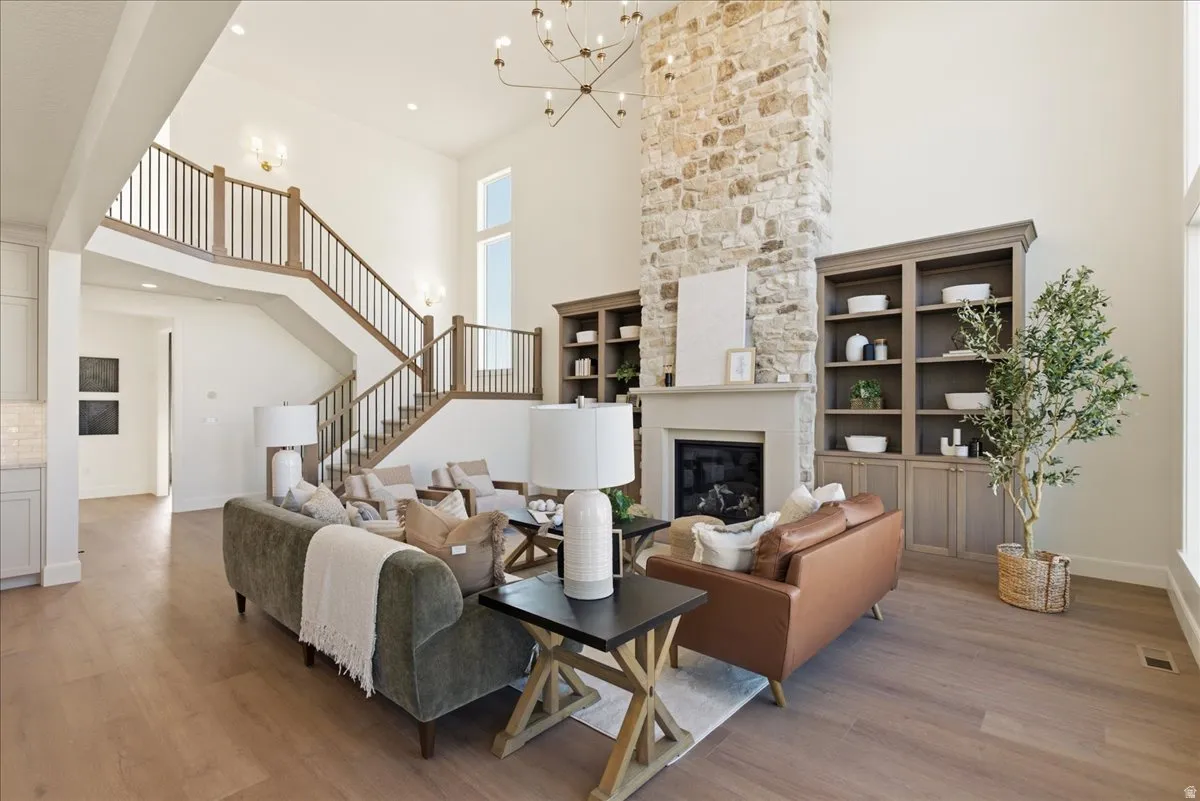 Two-story living area with a stone-clad fireplace, built-in shelving, wood-finish flooring, and a grand staircase featuring wood handrails and black balusters