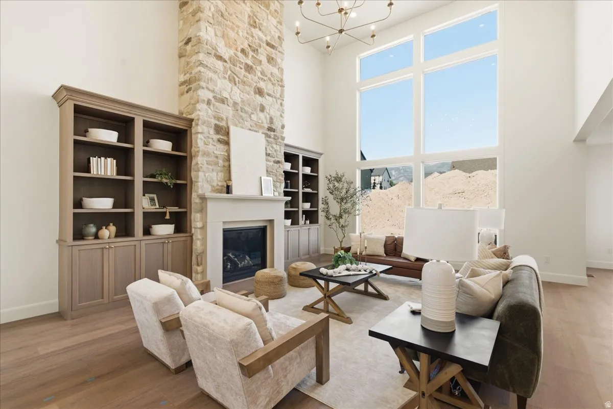 Living space featuring a stone fireplace with a light-colored mantel, built-in shelving, expansive windows, wood-finish flooring, and a decorative chandelier
