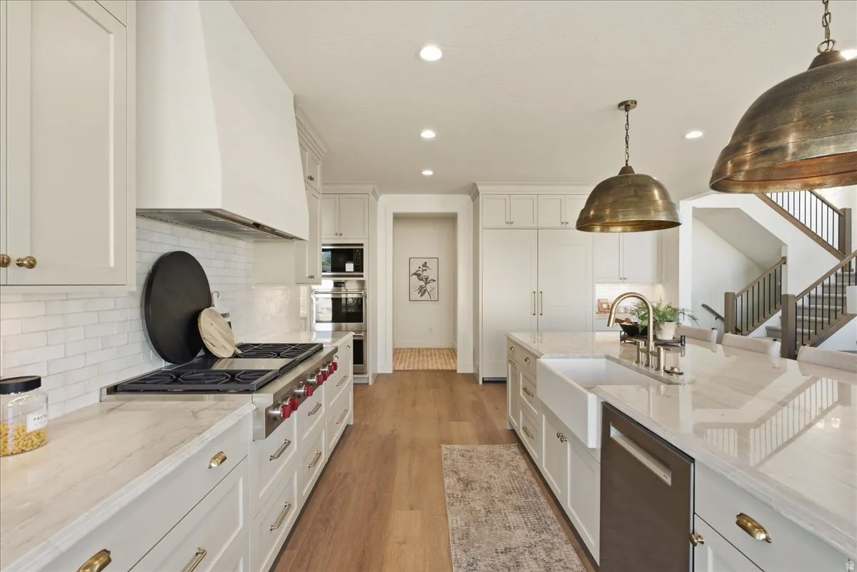 Spacious kitchen featuring an oversized island with a farm sink, professional-grade range with custom hood, integrated double ovens, and wood-finish flooring