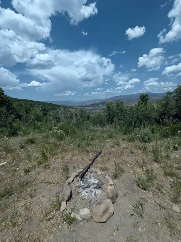 Expansive outdoor space featuring a rock-lined fire pit and natural foliage, with distant mountain ranges under a partly cloudy sky