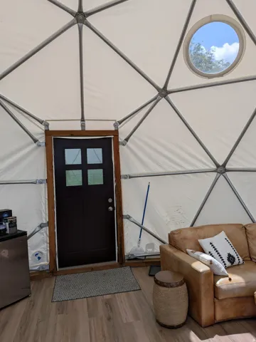 Geodesic dome interior featuring a white fabric membrane, exposed structural framework, and wood-finish flooring