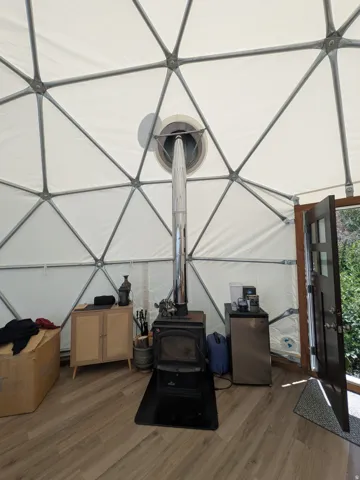 Geodesic dome interior featuring a central wood-burning stove with a metal flue