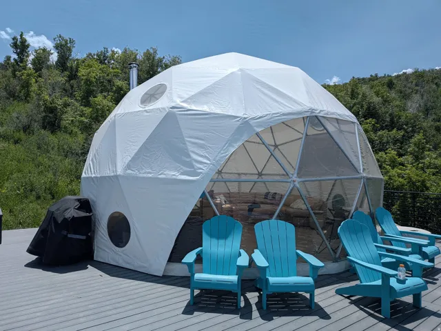 Geodesic dome structure featuring a partial transparent wall and a metal chimney