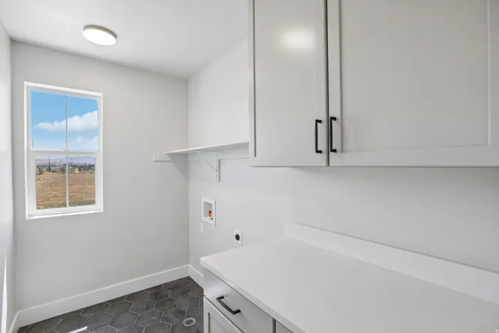 Dedicated laundry space featuring white cabinetry with black hardware, a light-toned countertop, and a utility sink hookup