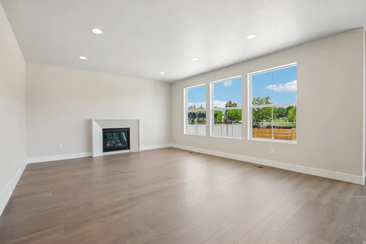 Spacious room featuring wood-finish flooring, a modern fireplace with a clean-line surround, and three large windows providing abundant natural light